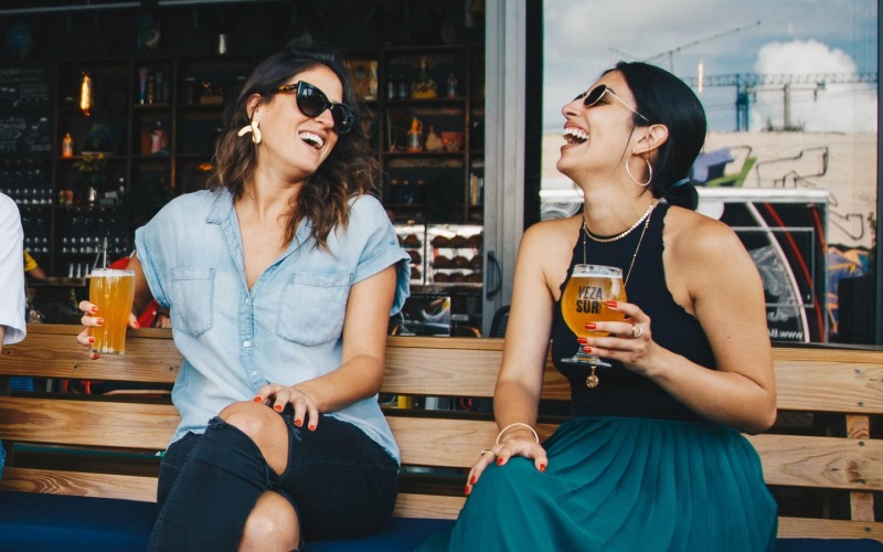 women with beers sitting on a bench in front of local restaurant